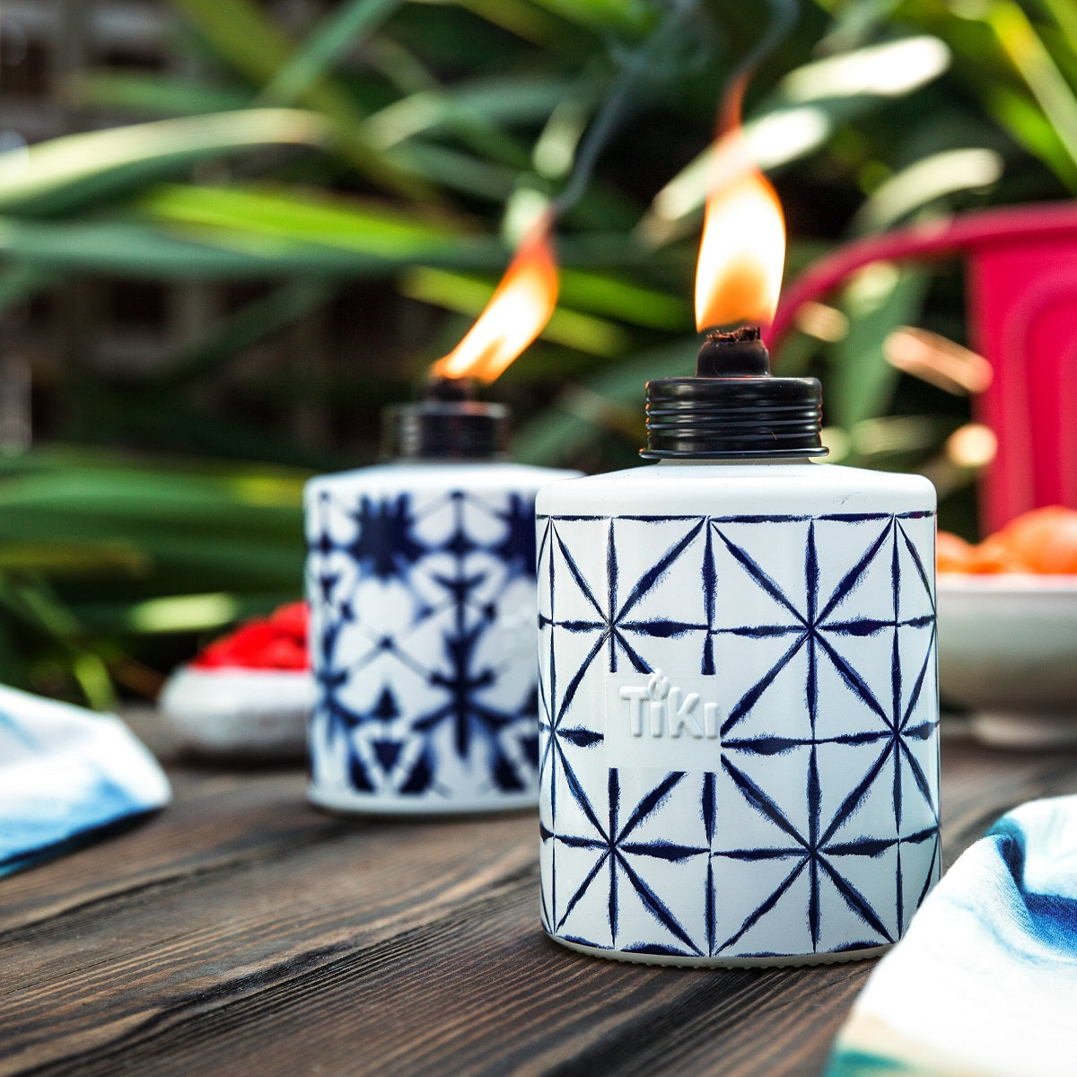White Tiki torch with blue geometric pattern, burning flame, outdoor setting.