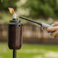 Black portable torch with flame, handheld igniter in use outdoors.