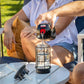 Black and red portable coffee maker pouring into glass mug on white table.