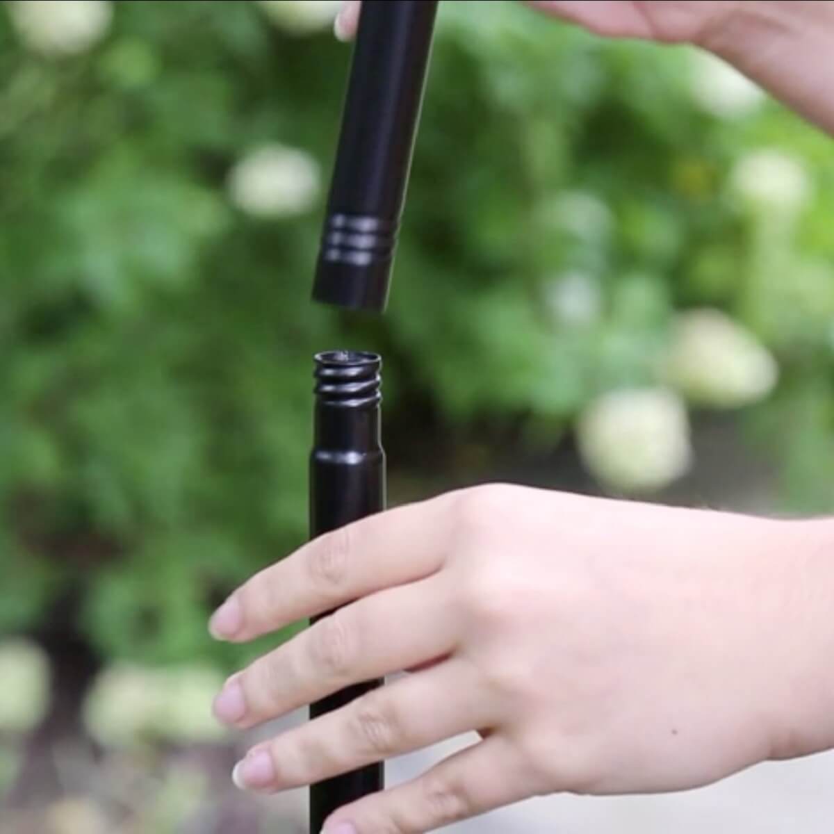 Black portable water filter with hand holding cap, outdoor setting.