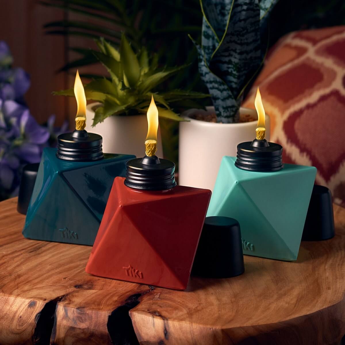 Colorful Tiki oil lamps in blue, red, and teal with lit flames, on a wooden surface.