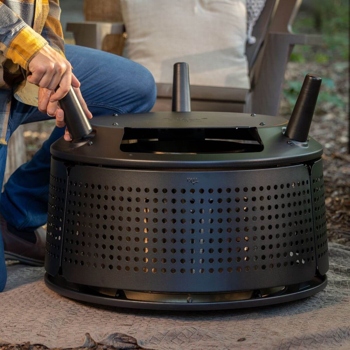 Black outdoor fire pit with perforated design and handle, modern style.