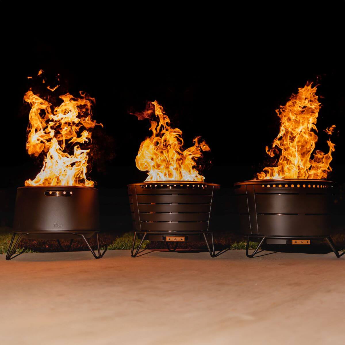 Three black fire pits with vibrant flames, set outdoors on a patio.