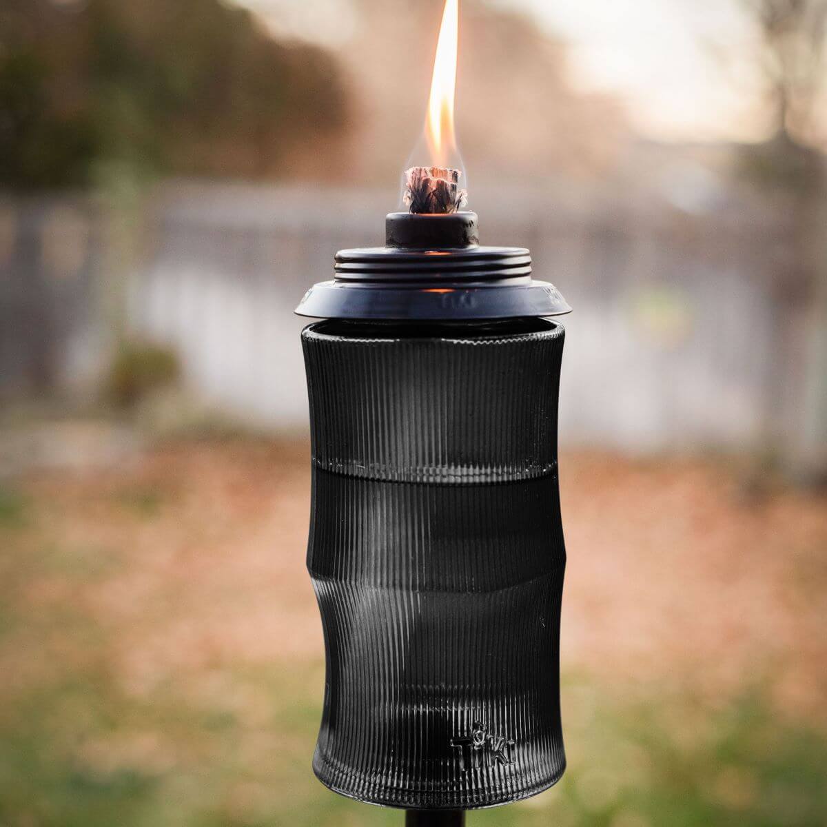 Black outdoor torch with flame, ribbed design, and protective cover.