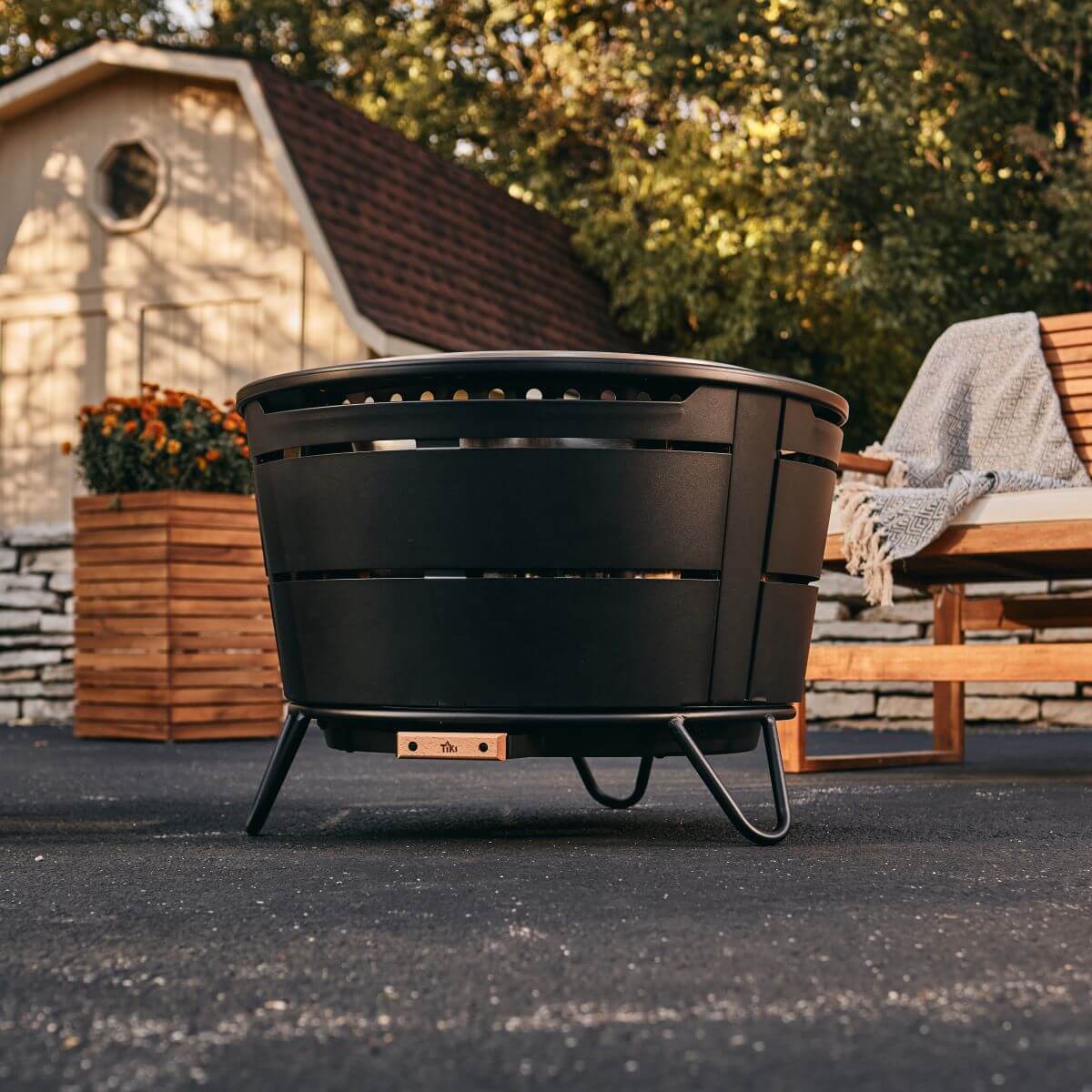 Black TIKI outdoor fire pit on stand, patio setting.