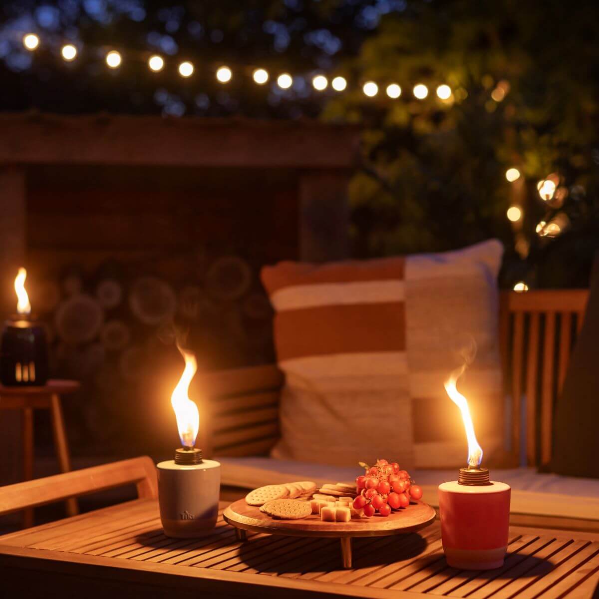 Candles and snacks on a wooden table outdoors at night.