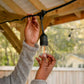 Black outdoor string light with clear bulb and orange filament, hanging from a wooden structure.