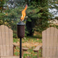 Black outdoor tiki torch with flame, set in backyard with chairs and table.