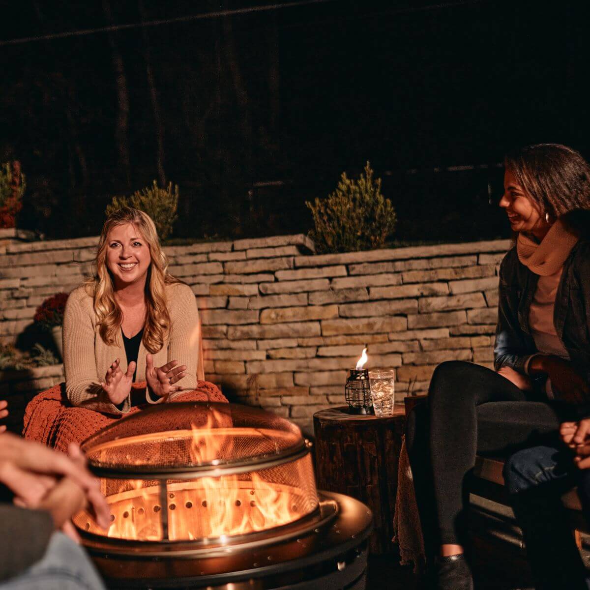 "Brass fire pit with mesh cover, glowing flames, outdoor setting."