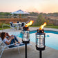 Black outdoor torches with glass cages and bright flames, near a poolside setting.