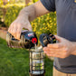Black portable lantern being refueled with liquid fuel outdoors.