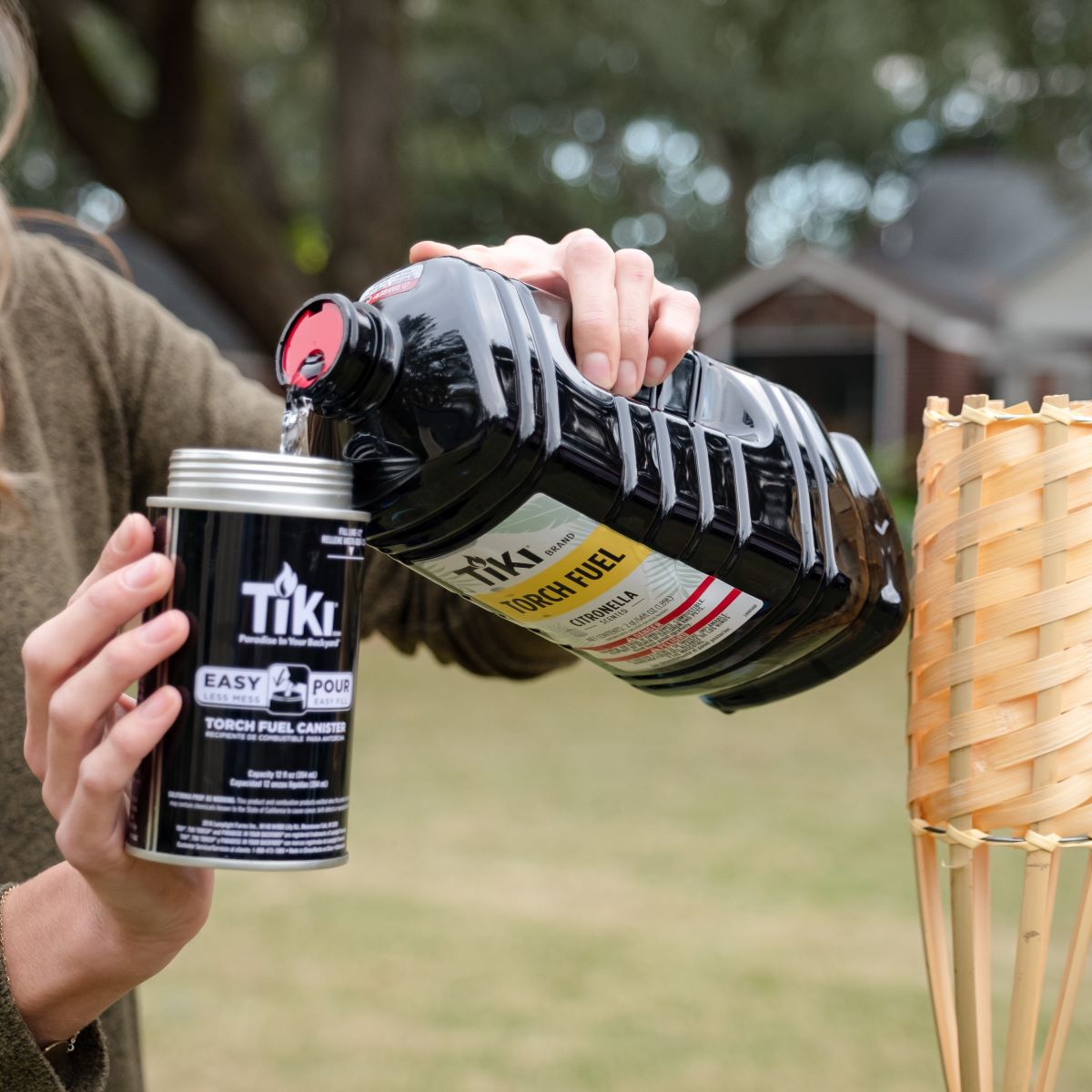 Black TIKI torch fuel bottle being poured into a canister.