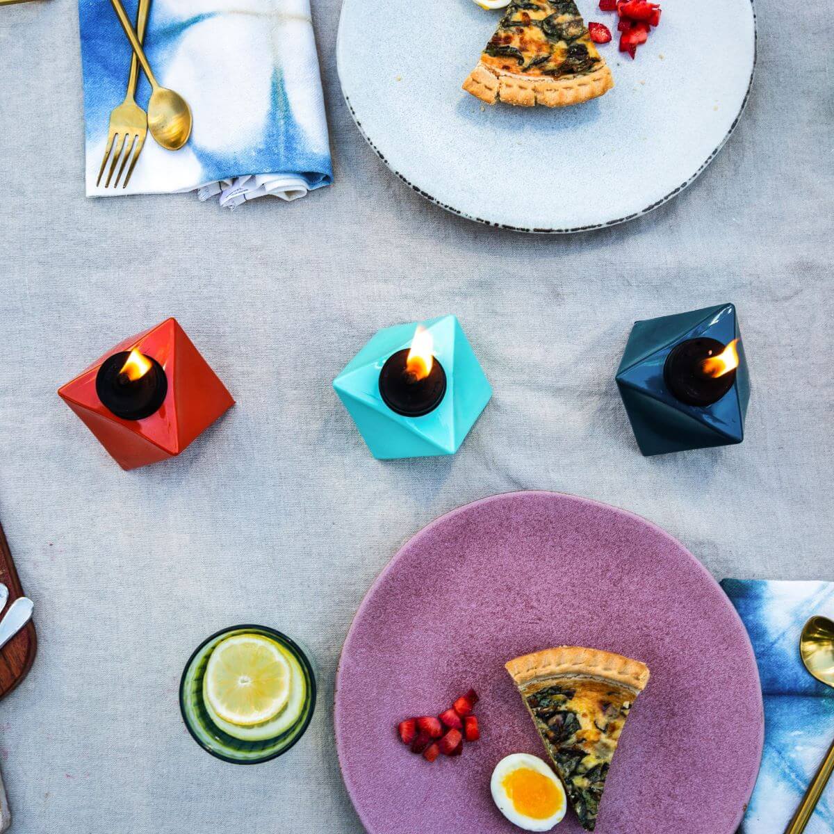 Colorful geometric candles with flame, set on a table with plates and food.