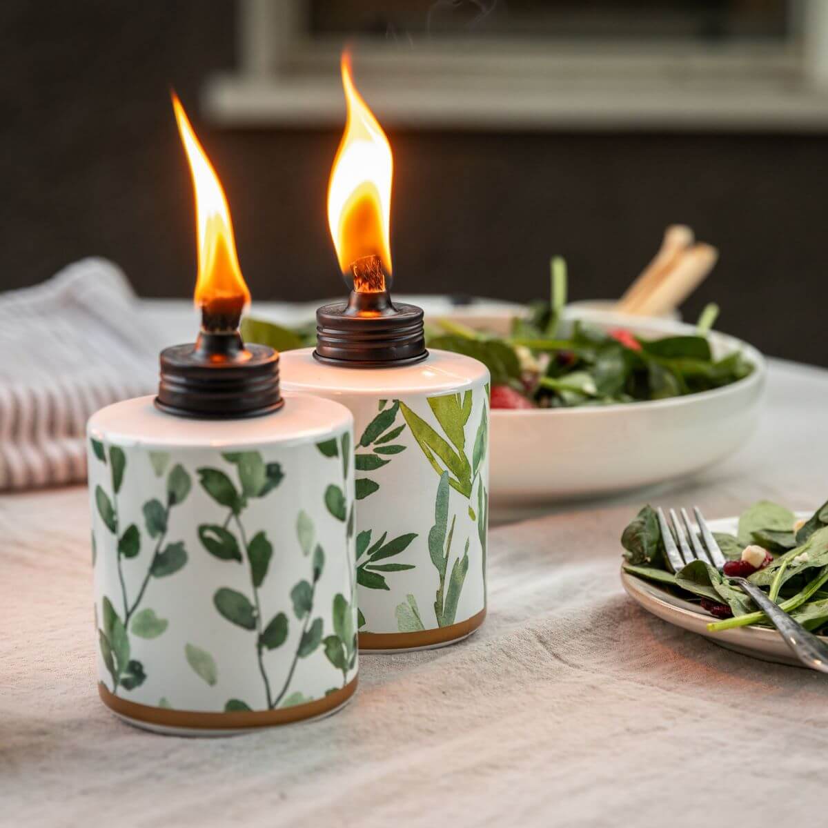 White ceramic oil burners with green leaf pattern, lit flames.