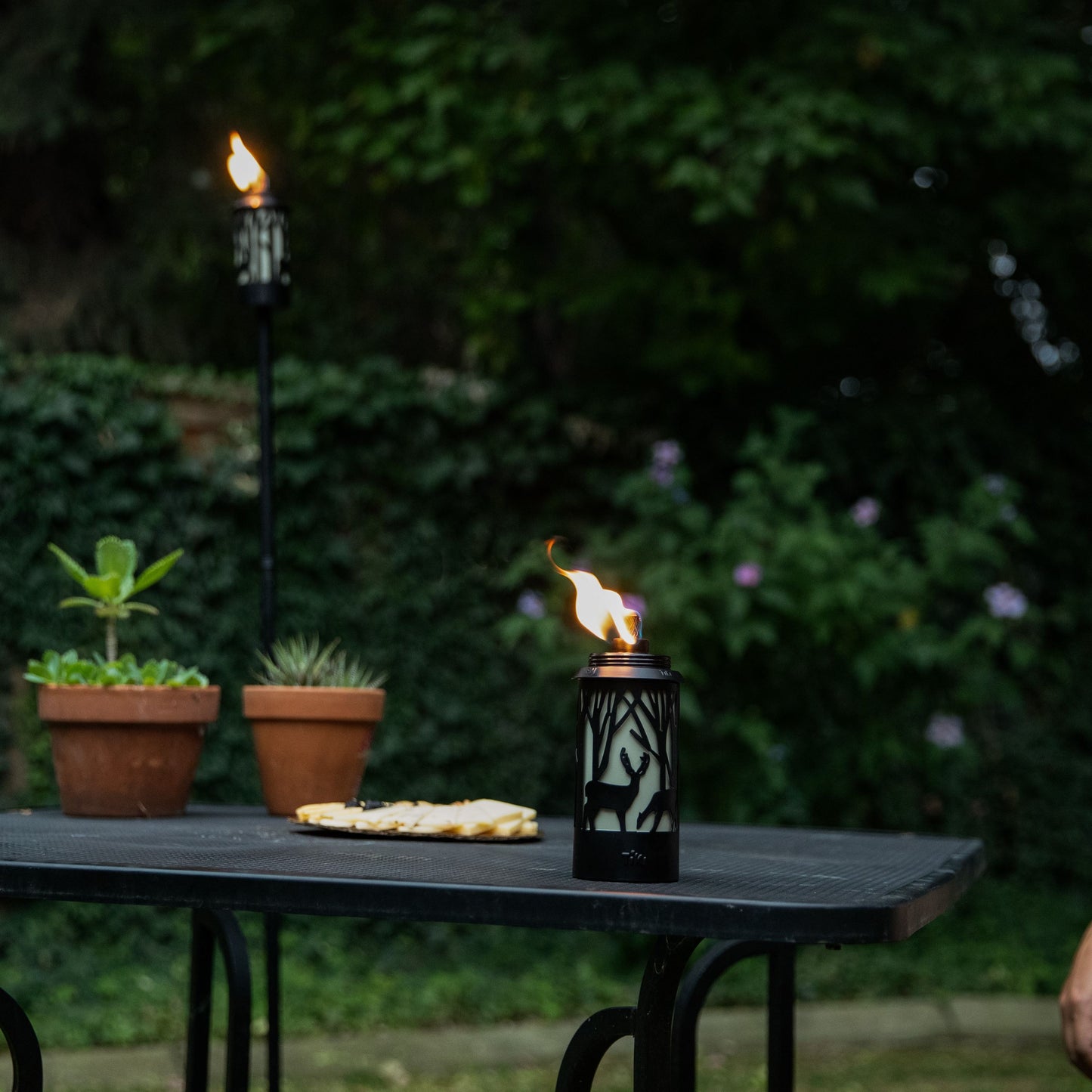 Black portable torch with deer design, lit on outdoor table.