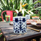 White ceramic tiki torch with blue geometric pattern, lit flame, outdoor setting.