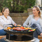 Black portable grill with sausages and vegetables cooking outdoors.