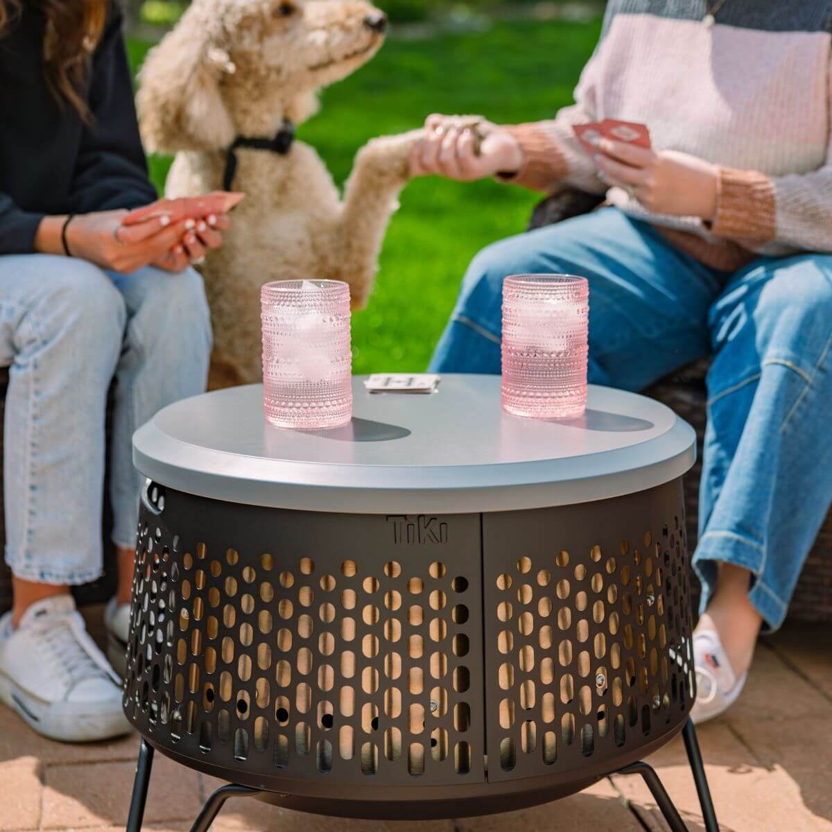 Gray Tiki outdoor coffee table with perforated design and pink glasses.