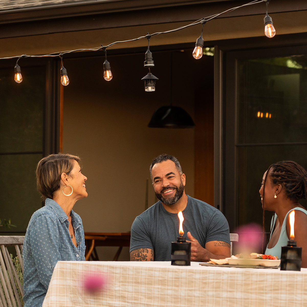 Outdoor string lights with vintage bulbs hang above a patio table set for dining, creating a warm, inviting ambiance.