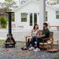 Black outdoor wood-burning chiminea with couple sitting nearby.