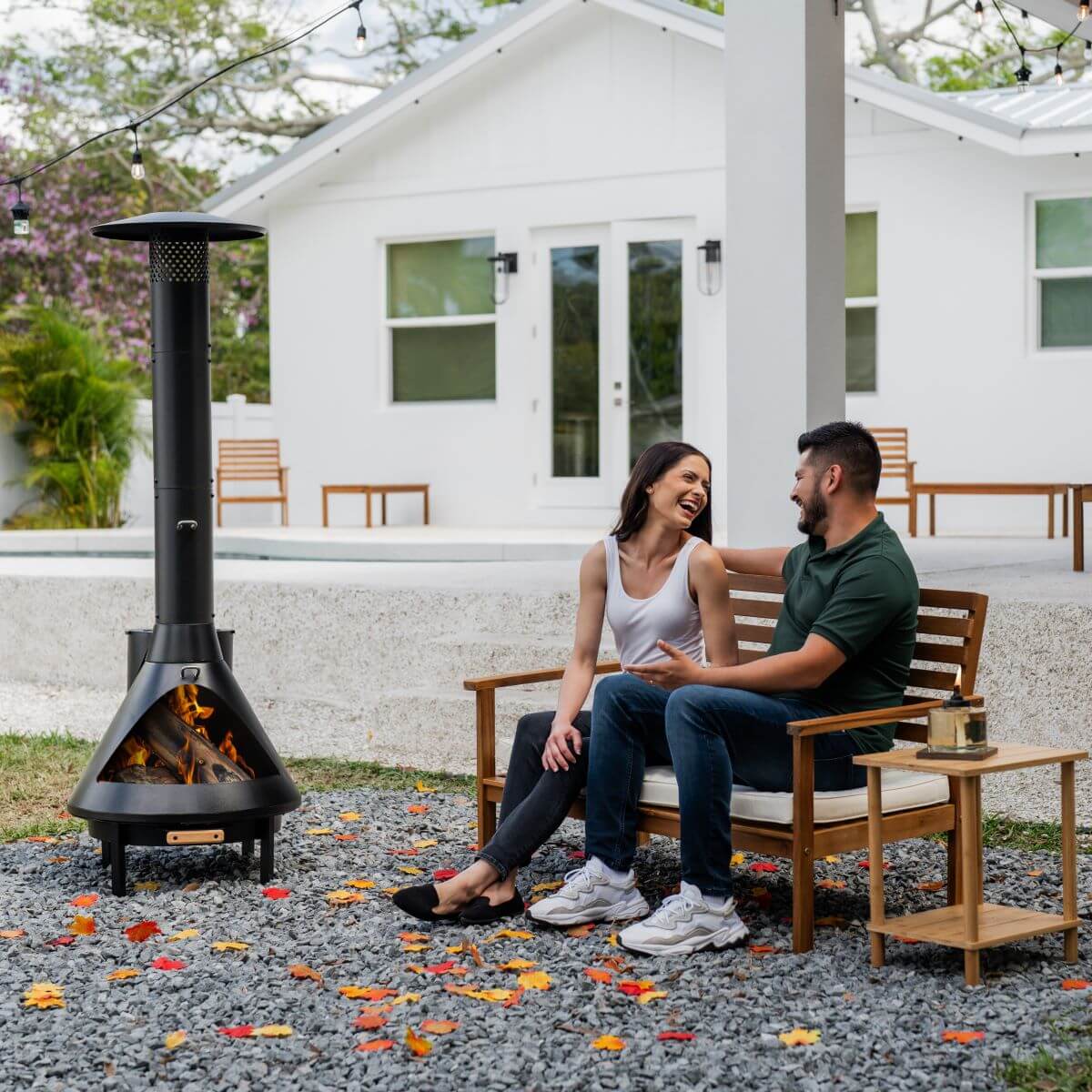 Black outdoor wood-burning chiminea with couple sitting nearby.