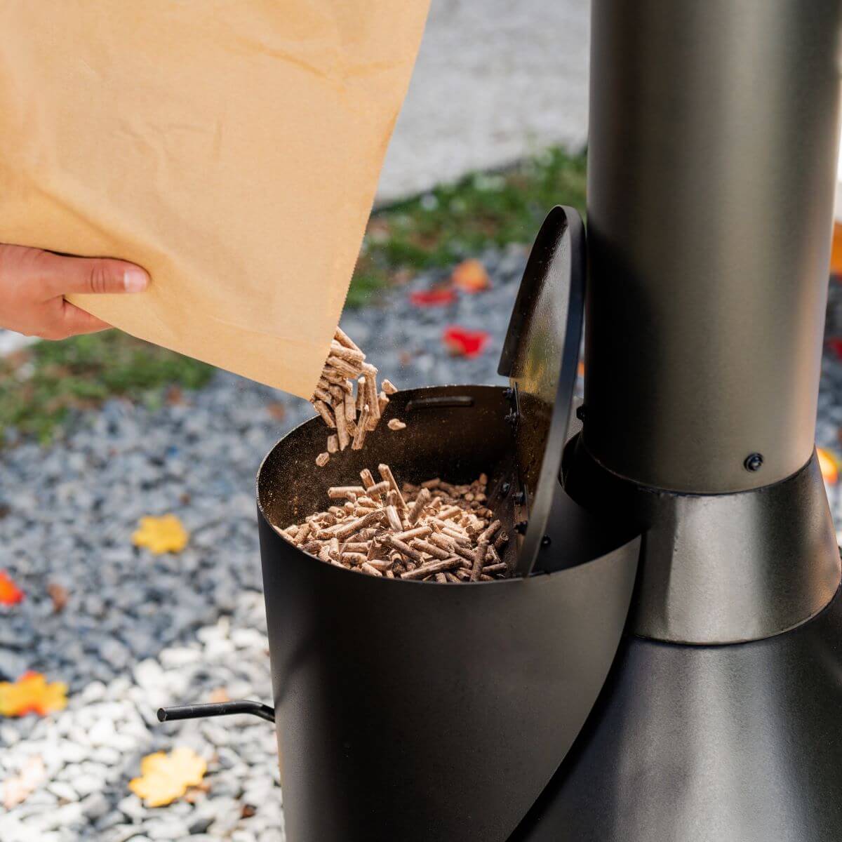 Black wood pellet smoker with person adding pellets.