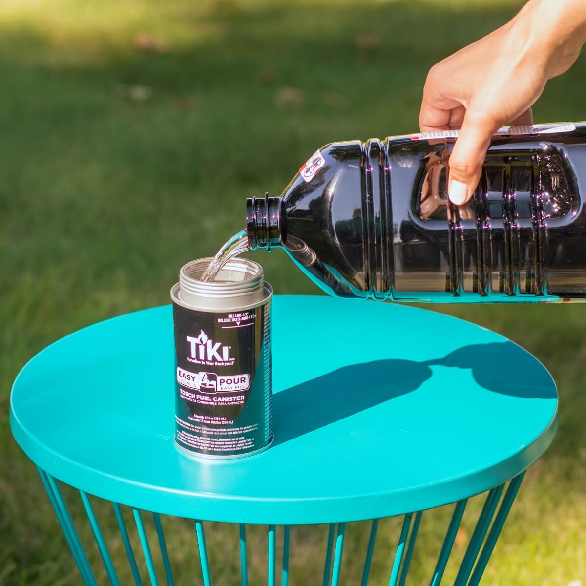 Green TIKI torch fuel canister being filled with liquid on a teal table.