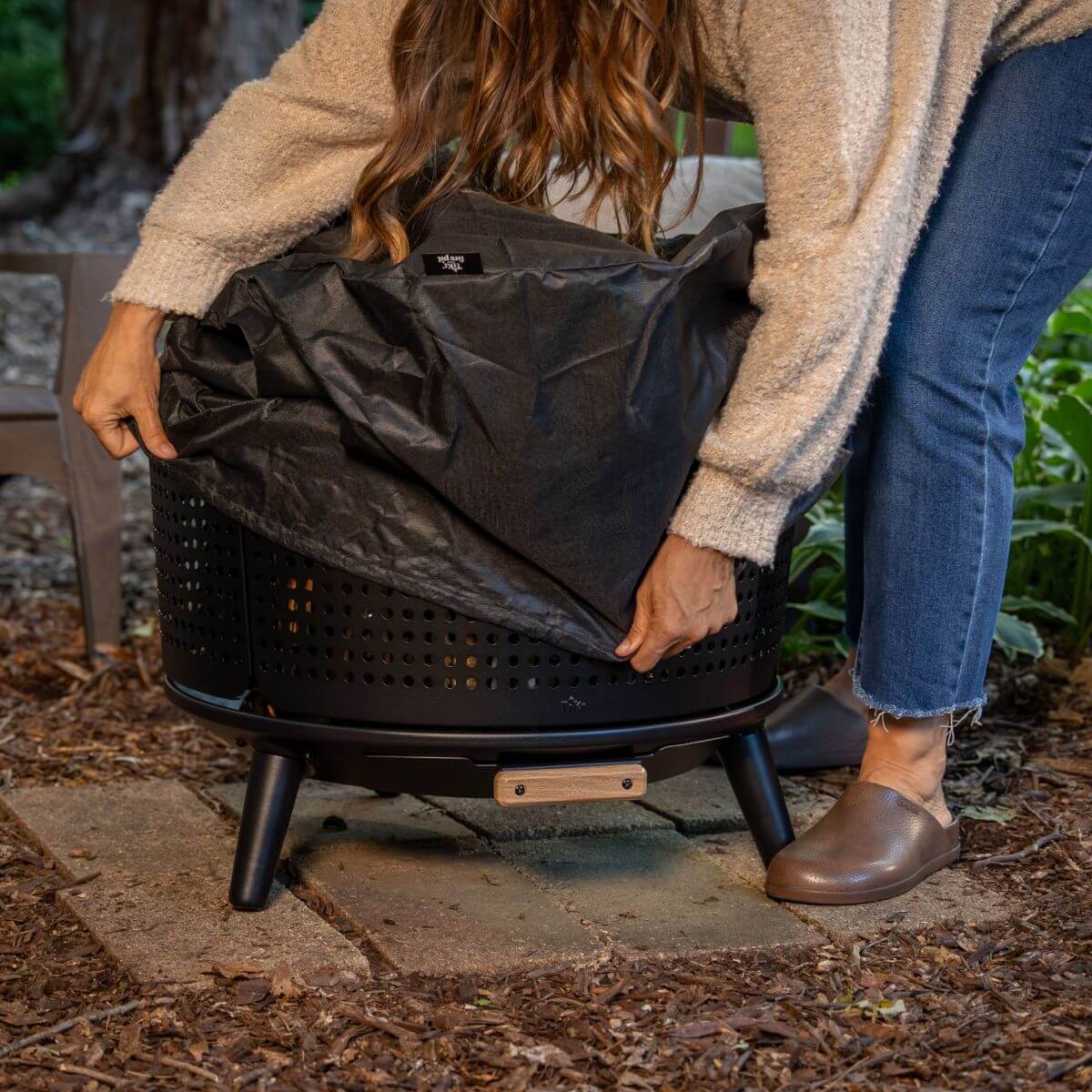 Black portable fire pit with protective cover being placed on it.