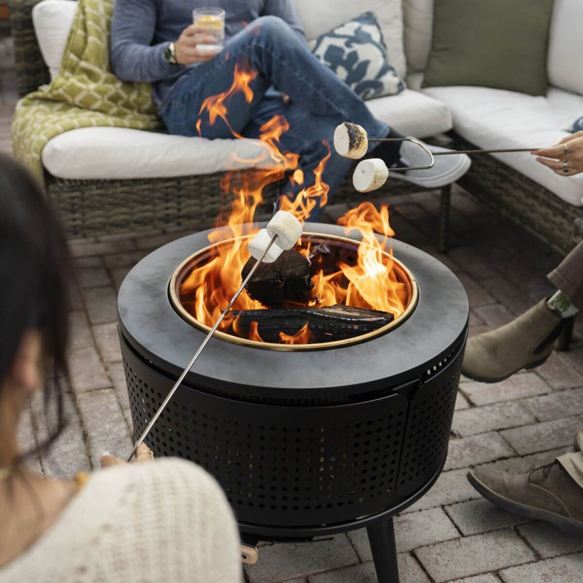 Black round fire pit with flames, people roasting marshmallows.