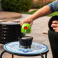 Green fuel container pouring liquid into blue fire pit burner on mosaic table.
