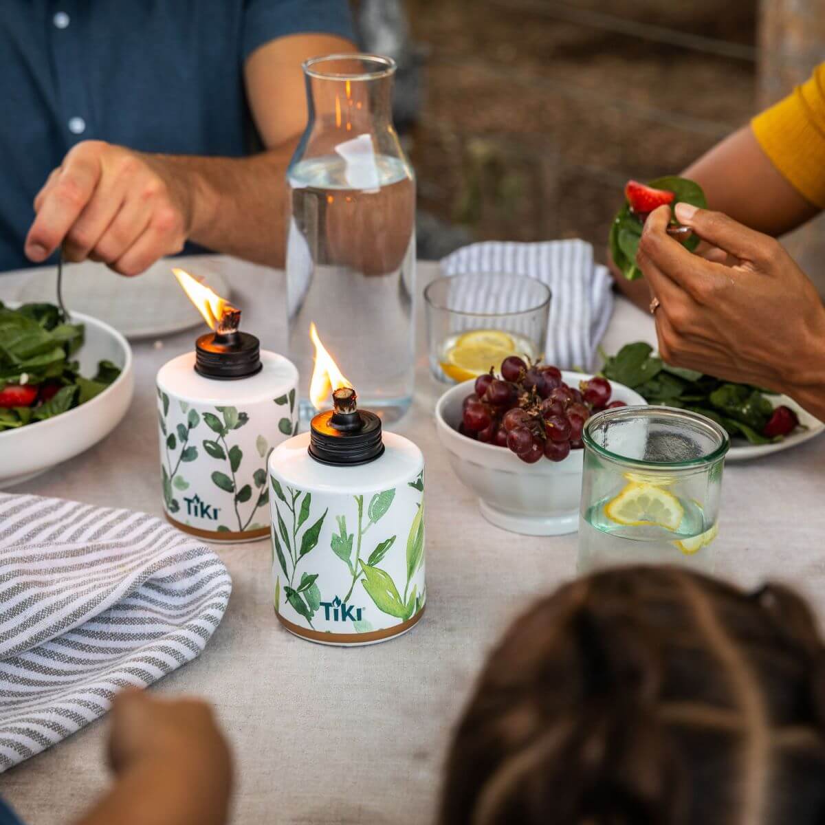 White Tiki oil lamps with green leaf design, lit on dining table.